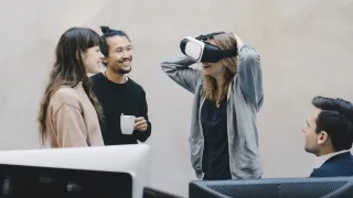 Nainen VR-lasit päässä juttelee kollegoilleen