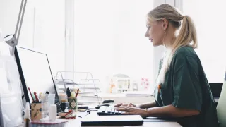 Henkilö istuu työpöydän ääressä tietokoneella. 